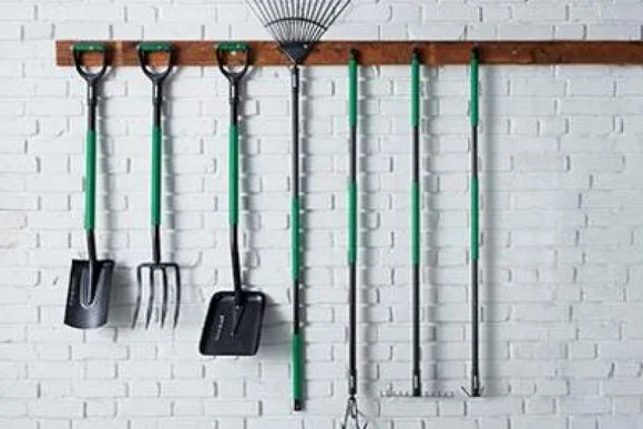 Verschiedene Gartengeräte hängen an einer weißen Ziegelwand.